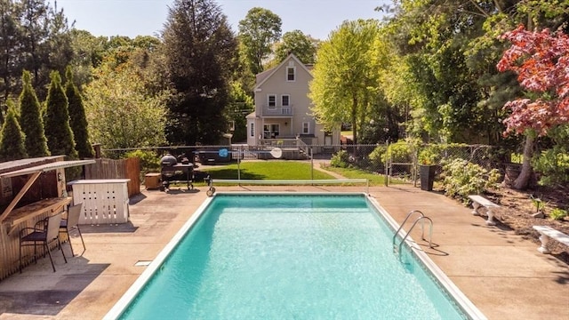 view of swimming pool featuring fence, a patio area, and view of wooded area