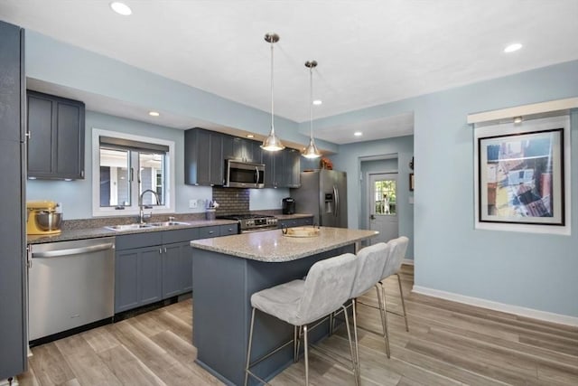 kitchen with appliances with stainless steel finishes, a sink, a kitchen bar, light wood-style flooring, and a center island