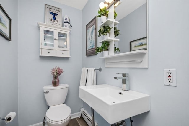 half bath featuring a sink, toilet, baseboards, baseboard heating, and wood finished floors