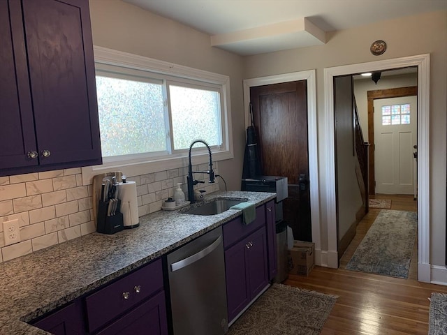 kitchen with stainless steel dishwasher, a sink, backsplash, wood finished floors, and stone countertops