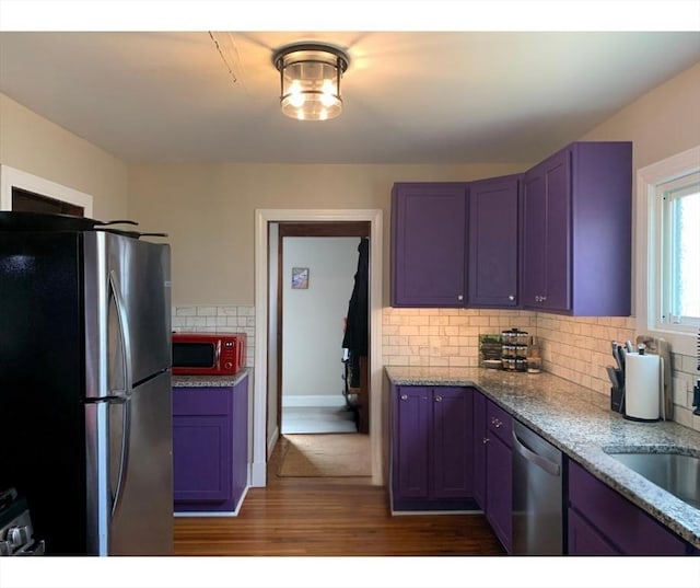 kitchen with stainless steel appliances, dark wood-style flooring, tasteful backsplash, light stone countertops, and a sink