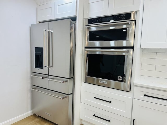 kitchen with stainless steel appliances, light countertops, decorative backsplash, light wood-style floors, and white cabinetry