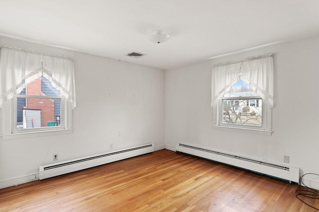 empty room with a baseboard heating unit, light wood-type flooring, and visible vents