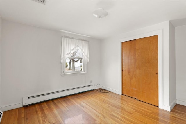 unfurnished bedroom with baseboards, baseboard heating, and wood finished floors