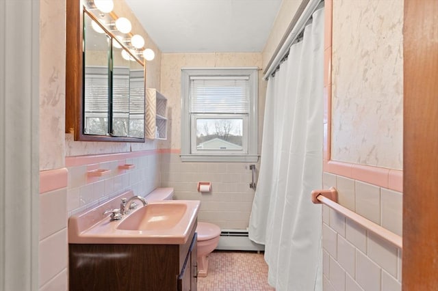 bathroom with toilet, a wainscoted wall, baseboard heating, vanity, and tile walls