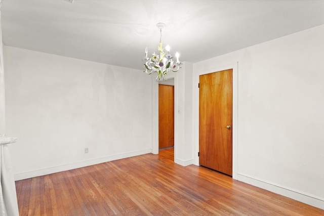 unfurnished room featuring a chandelier, wood finished floors, and baseboards