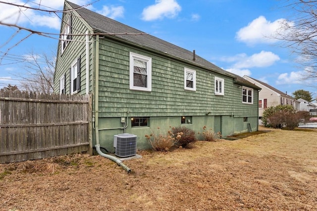 rear view of property featuring a lawn, fence, and central air condition unit