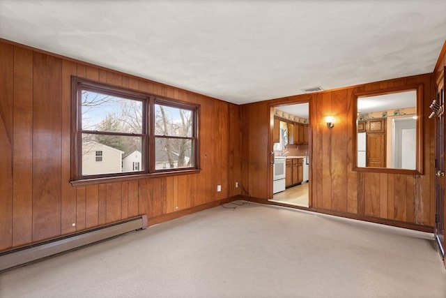 spare room with light colored carpet, visible vents, baseboard heating, wooden walls, and baseboards