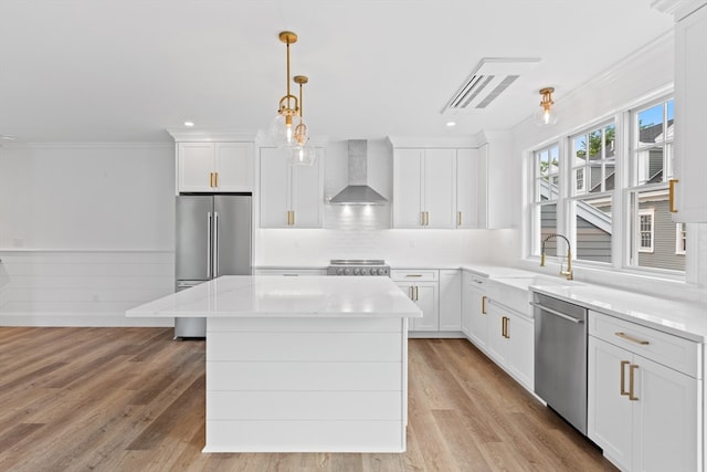 kitchen featuring a center island, appliances with stainless steel finishes, white cabinetry, a sink, and wall chimney range hood