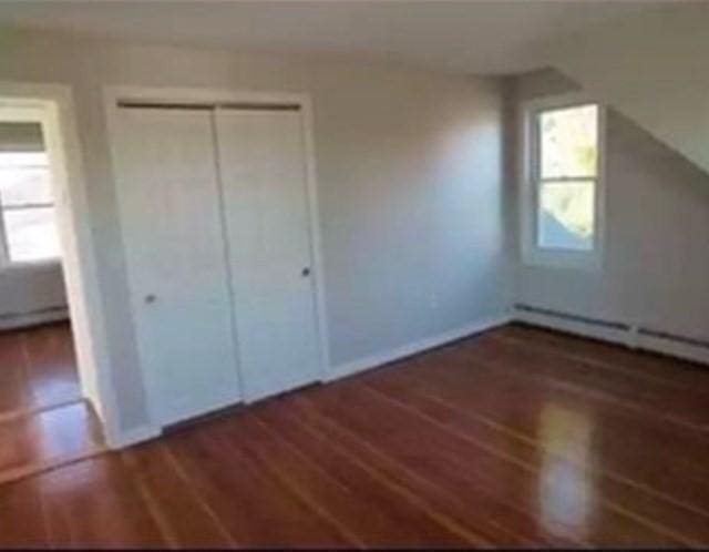 unfurnished bedroom with a baseboard heating unit, dark wood-type flooring, and a closet