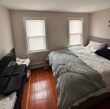 bedroom with dark wood-type flooring, multiple windows, and a baseboard heating unit