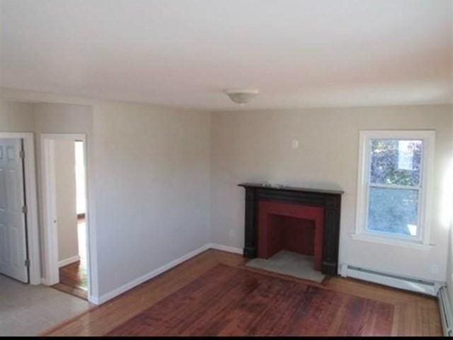 unfurnished living room featuring wood-type flooring and a baseboard heating unit