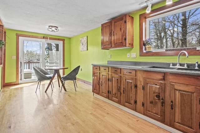 kitchen featuring dark countertops, a sink, brown cabinetry, and light wood-type flooring