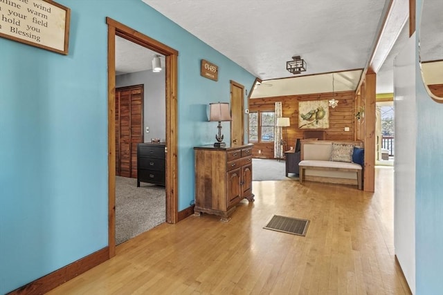 hallway with visible vents, wood walls, light wood finished floors, and baseboards