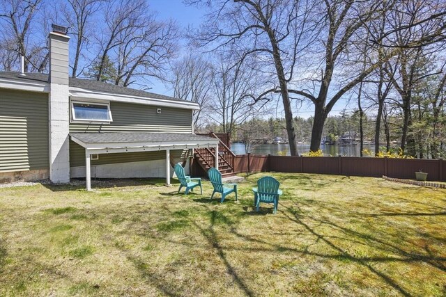 view of yard with fence, a deck with water view, and stairs