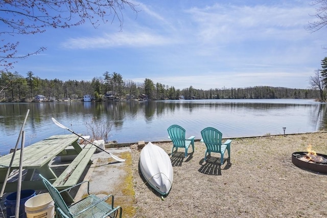 view of dock featuring a fire pit, a wooded view, and a water view