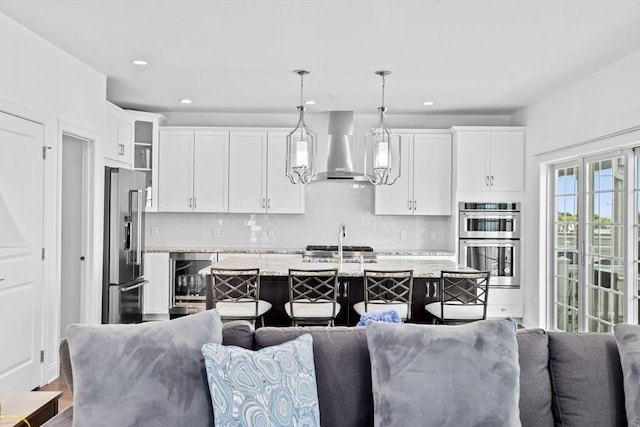 kitchen featuring pendant lighting, wall chimney exhaust hood, appliances with stainless steel finishes, light stone counters, and a breakfast bar area