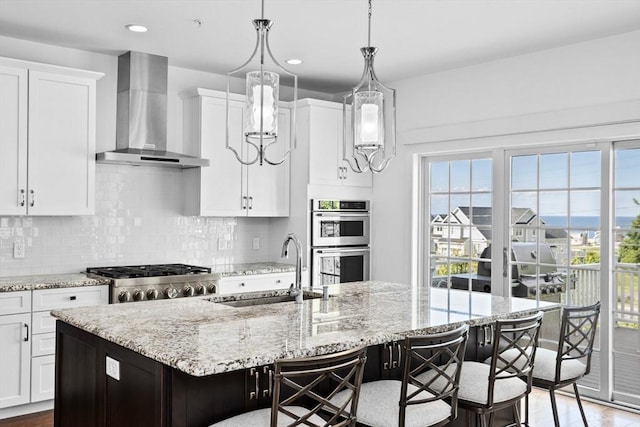 kitchen with double oven, a breakfast bar area, a spacious island, and wall chimney range hood