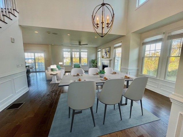 dining area with ceiling fan with notable chandelier, a healthy amount of sunlight, and dark hardwood / wood-style flooring