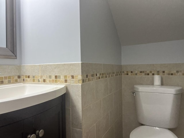 bathroom with vanity, lofted ceiling, tile walls, and toilet