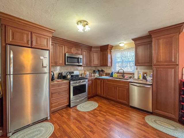 kitchen featuring hardwood / wood-style flooring, stainless steel appliances, tasteful backsplash, a textured ceiling, and sink