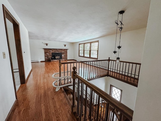 corridor with baseboard heating, baseboards, an upstairs landing, and wood finished floors