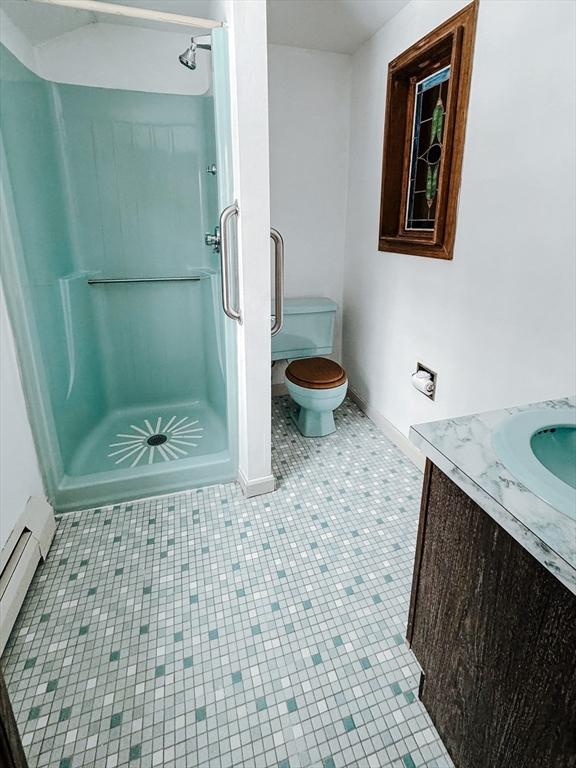 bathroom featuring a baseboard radiator, toilet, vanity, a shower stall, and baseboards