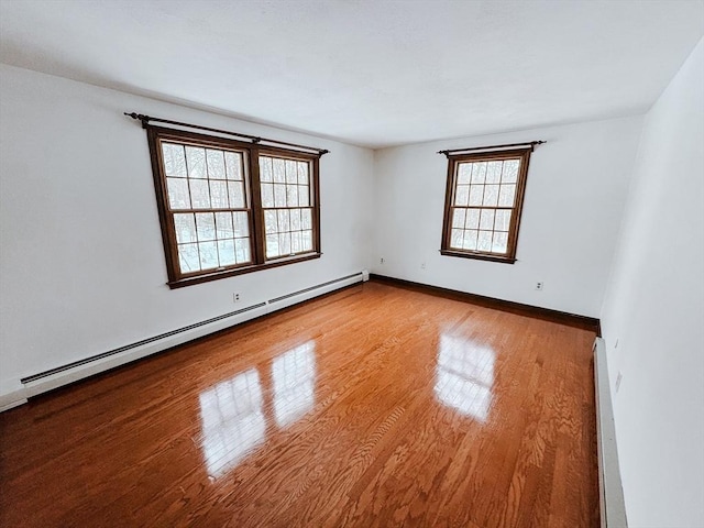 empty room featuring a baseboard radiator, baseboards, and light wood finished floors