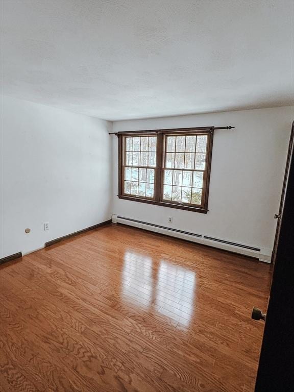 empty room with a baseboard heating unit, a textured ceiling, baseboards, and wood finished floors