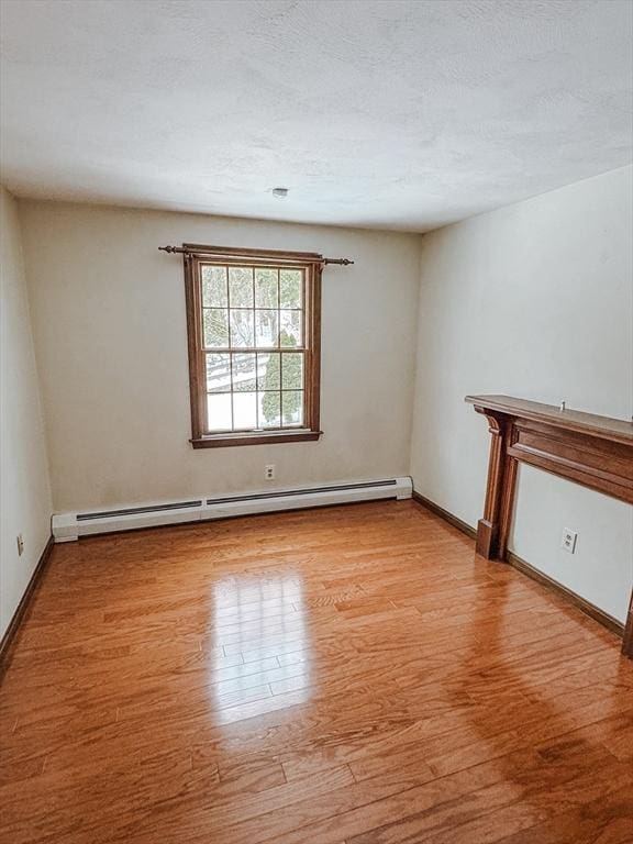 spare room featuring light wood-style floors, baseboards, baseboard heating, and a textured ceiling