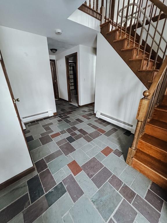 stairway with a baseboard heating unit, a baseboard radiator, baseboards, and stone tile floors