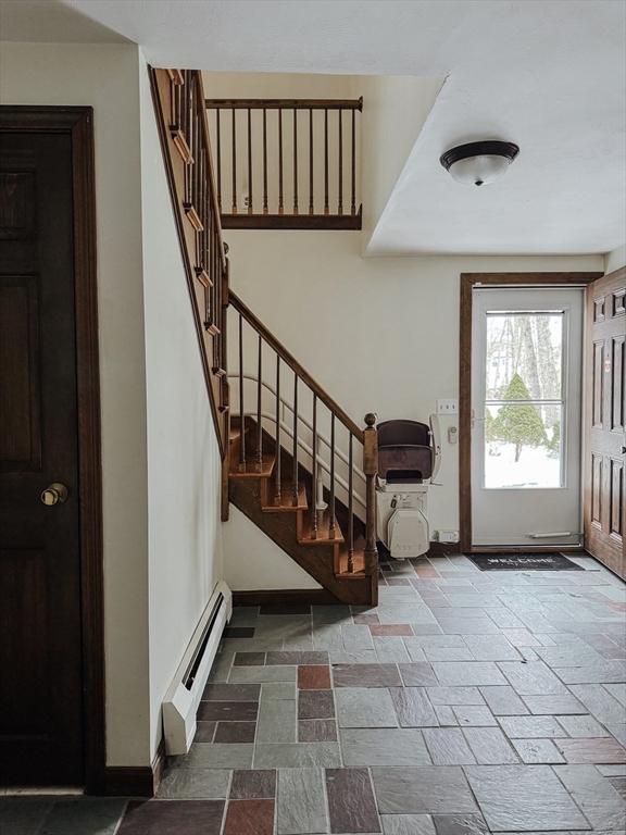 entrance foyer with stone finish floor, stairway, baseboards, and a baseboard heating unit