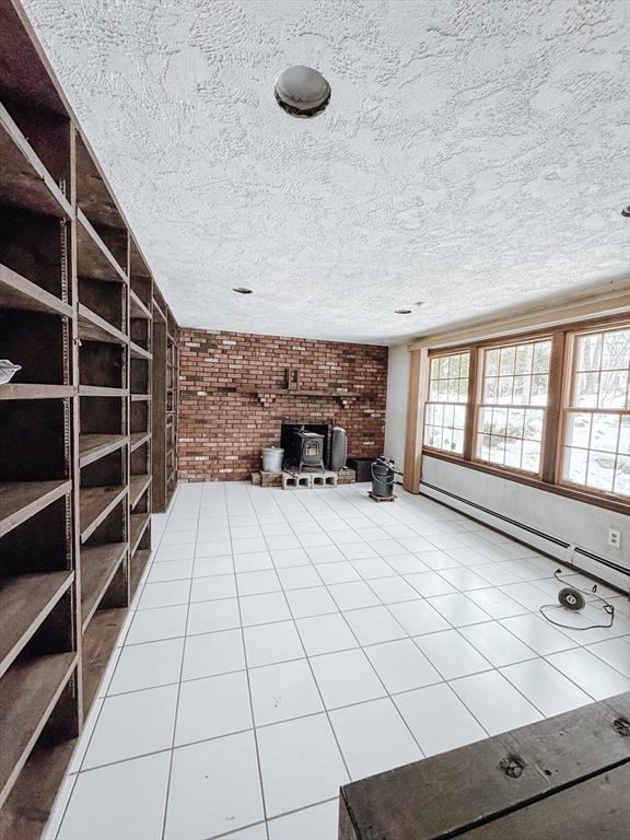 unfurnished living room with a baseboard heating unit, a wealth of natural light, a wood stove, and brick wall