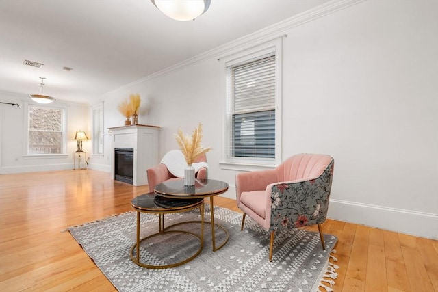 sitting room with crown molding, visible vents, wood finished floors, and a glass covered fireplace