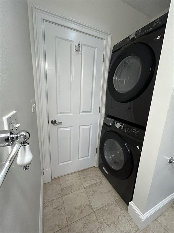laundry area with laundry area, stacked washer and dryer, baseboards, and marble finish floor