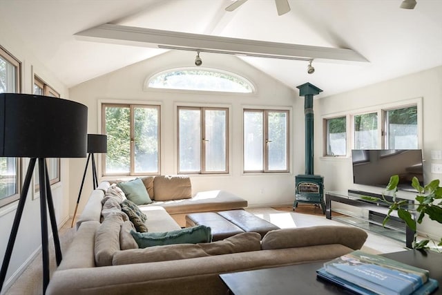 living area with a wood stove, baseboards, vaulted ceiling with beams, rail lighting, and a ceiling fan