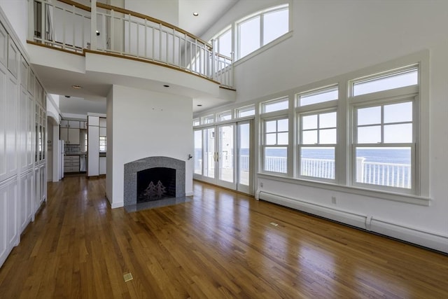 240 Atlantic Rd, Gloucester, MA 01930 - unfurnished living room featuring a baseboard heating unit, a fireplace with flush hearth, wood finished floors, and a towering ceiling