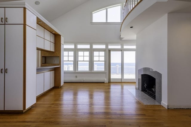 240 Atlantic Rd, Gloucester, MA 01930 - unfurnished living room featuring a fireplace with flush hearth, wood finished floors, high vaulted ceiling, and a baseboard radiator