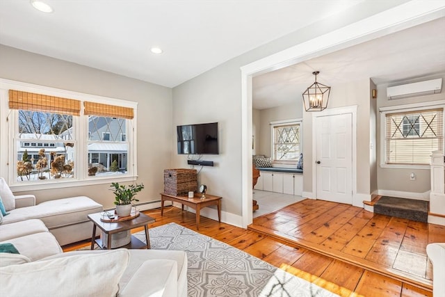 living area featuring baseboards, hardwood / wood-style flooring, a baseboard radiator, a wall mounted air conditioner, and a notable chandelier