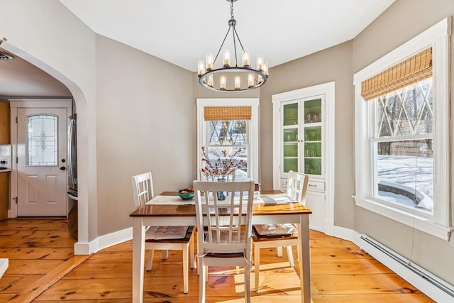 dining space featuring arched walkways, a notable chandelier, light wood finished floors, a baseboard radiator, and baseboards