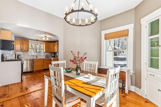 dining space with a chandelier, arched walkways, baseboards, and light wood finished floors