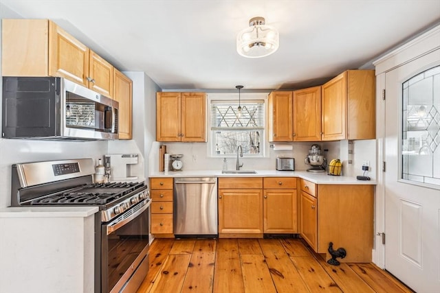 kitchen with light wood finished floors, decorative light fixtures, stainless steel appliances, light countertops, and a sink