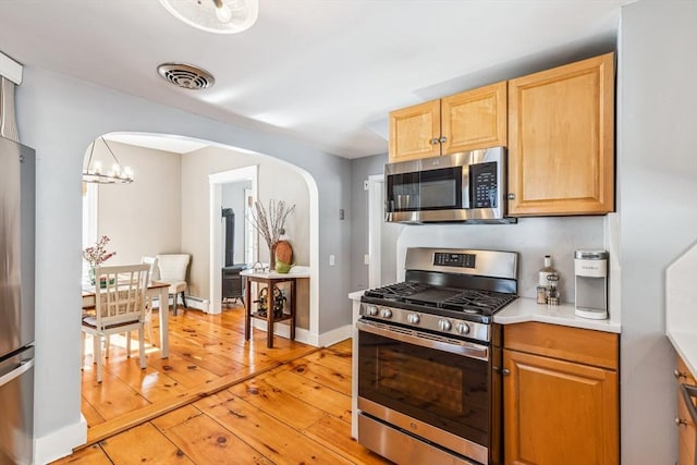 kitchen featuring visible vents, arched walkways, light wood-style flooring, stainless steel appliances, and light countertops