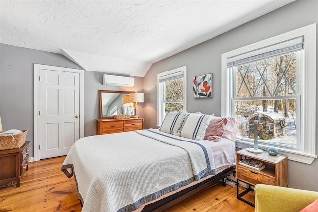 bedroom featuring lofted ceiling, an AC wall unit, a textured ceiling, and light wood-style floors