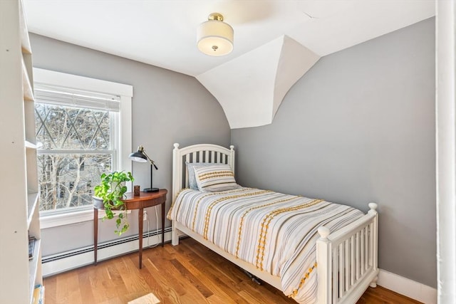 bedroom with vaulted ceiling, a baseboard radiator, wood finished floors, and baseboards