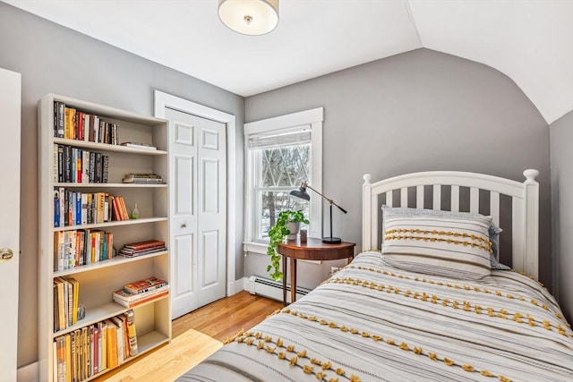 bedroom with a baseboard heating unit, lofted ceiling, a closet, and wood finished floors