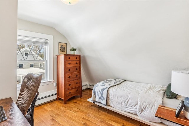 bedroom featuring a baseboard heating unit, lofted ceiling, and light wood finished floors