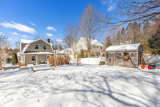 snow covered property with an outbuilding, a chimney, fence, and a gambrel roof