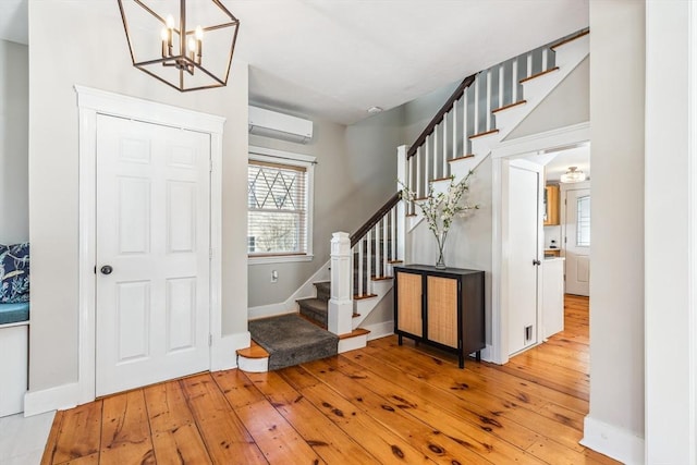 entrance foyer featuring wood-type flooring, an inviting chandelier, a wall mounted AC, baseboards, and stairs