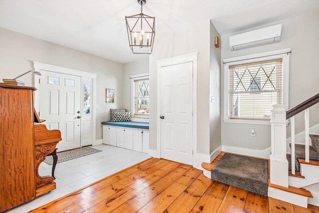 foyer entrance with a wall unit AC, a notable chandelier, baseboards, stairway, and light wood finished floors